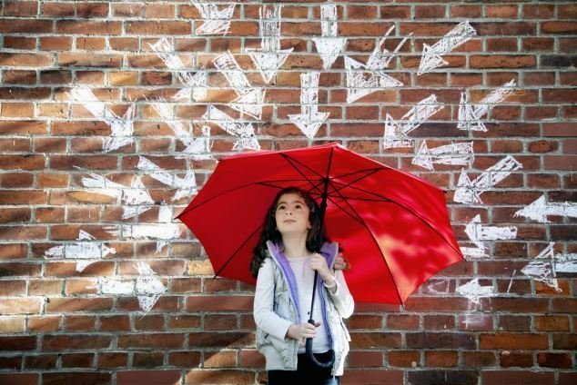 Young girl with red umbrella in front of brick wall surrounded by arrows